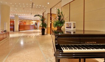 Un'ampia hall d'hotel con un pianoforte a coda, una reception e piante in vaso.