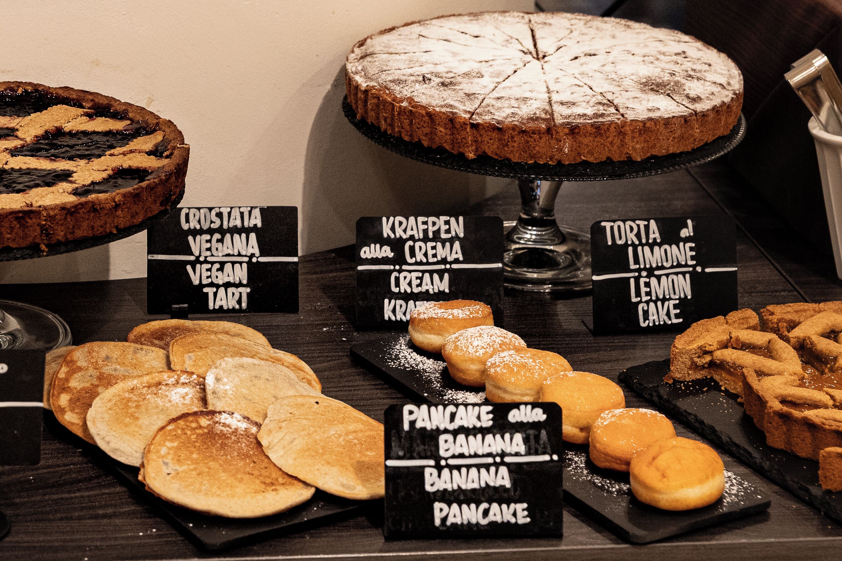 A dessert display with various cakes and pastries, including a lemon cake and banana pancakes.