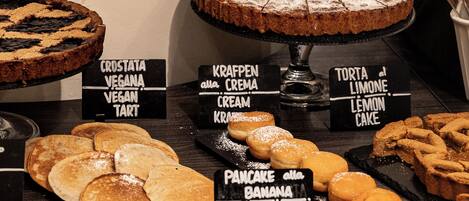 A dessert display with various cakes and pastries, including a lemon cake and banana pancakes.