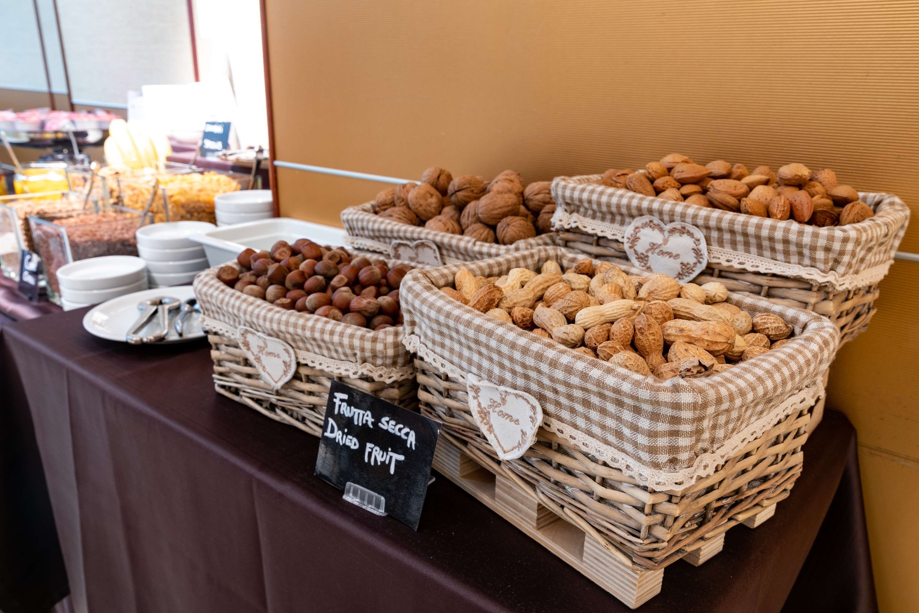 A buffet table with various food items, including baskets of nuts and dried fruits, and a sign indicating 'FRUTTA SECCA DRIED FRUIT'.
