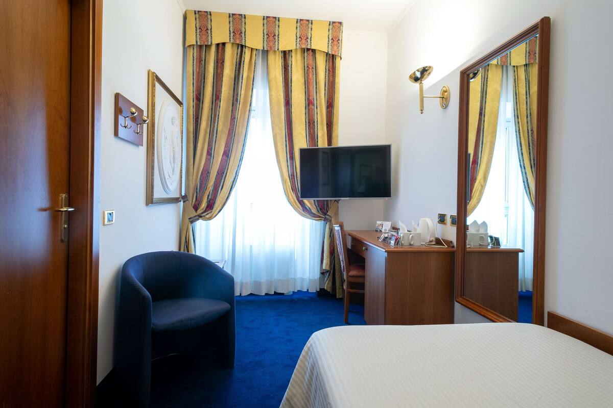 A hotel room with a bed, a desk, a chair, a television, and curtains.