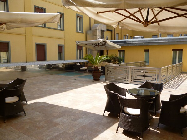 Un patio al aire libre con mobiliario de mimbre, sombrillas y una zona de piscina.