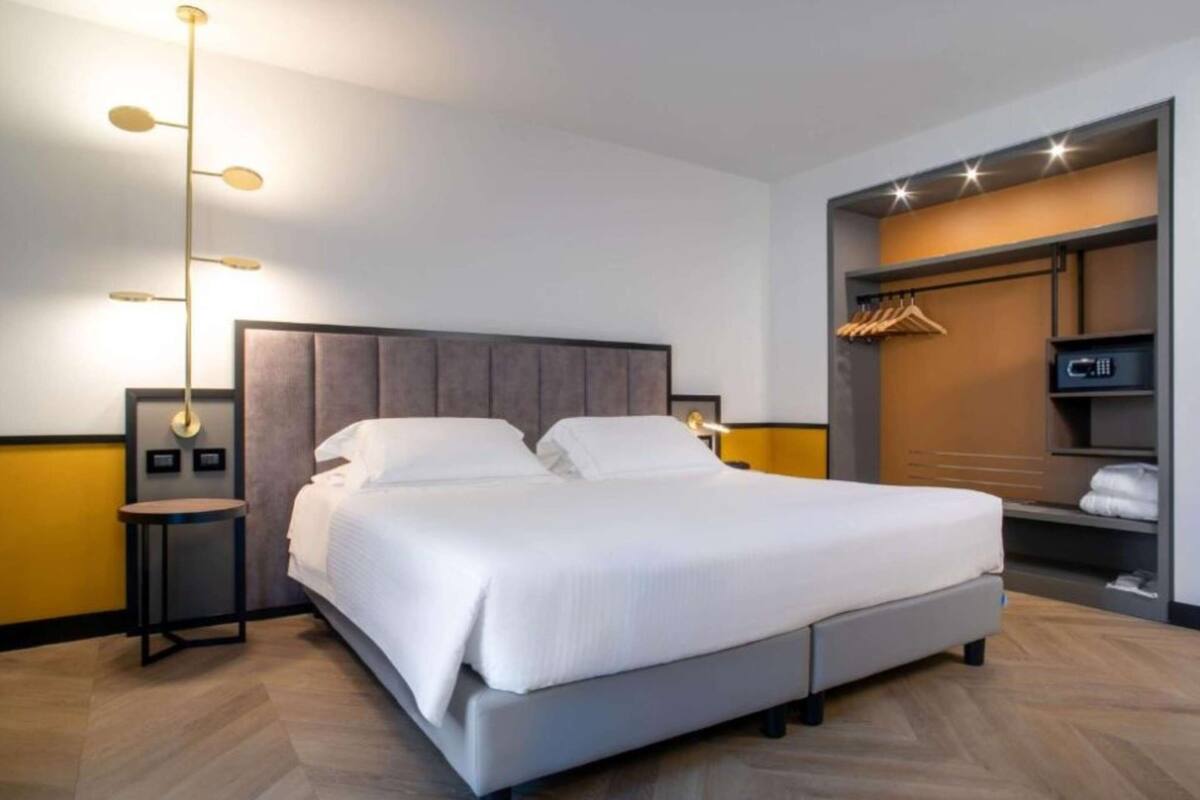 A modern hotel room with a large bed, a bedside table, a wardrobe, and a hanging closet.