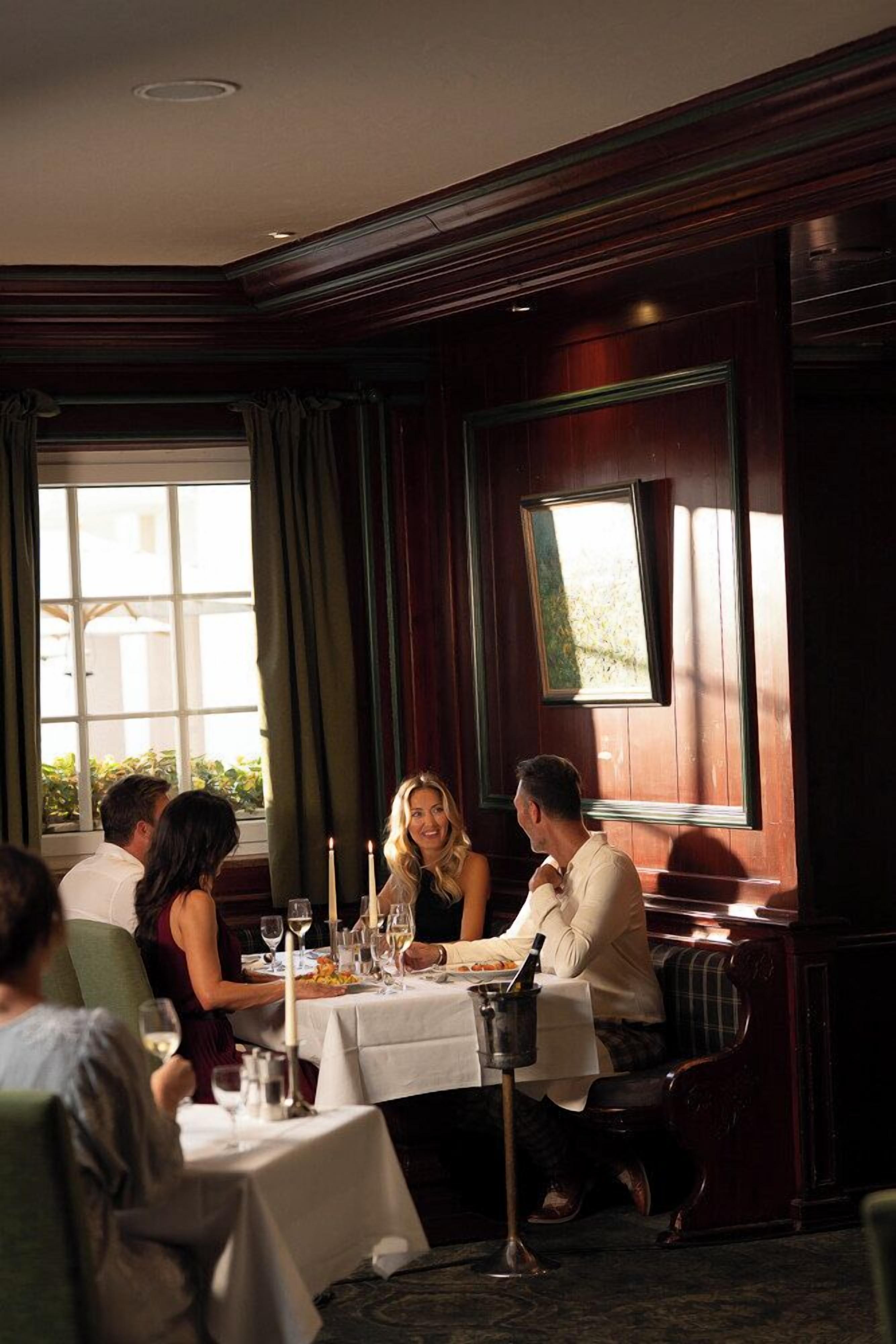 A dining area with a table set for four people, a window with curtains, and a framed picture on the wall.