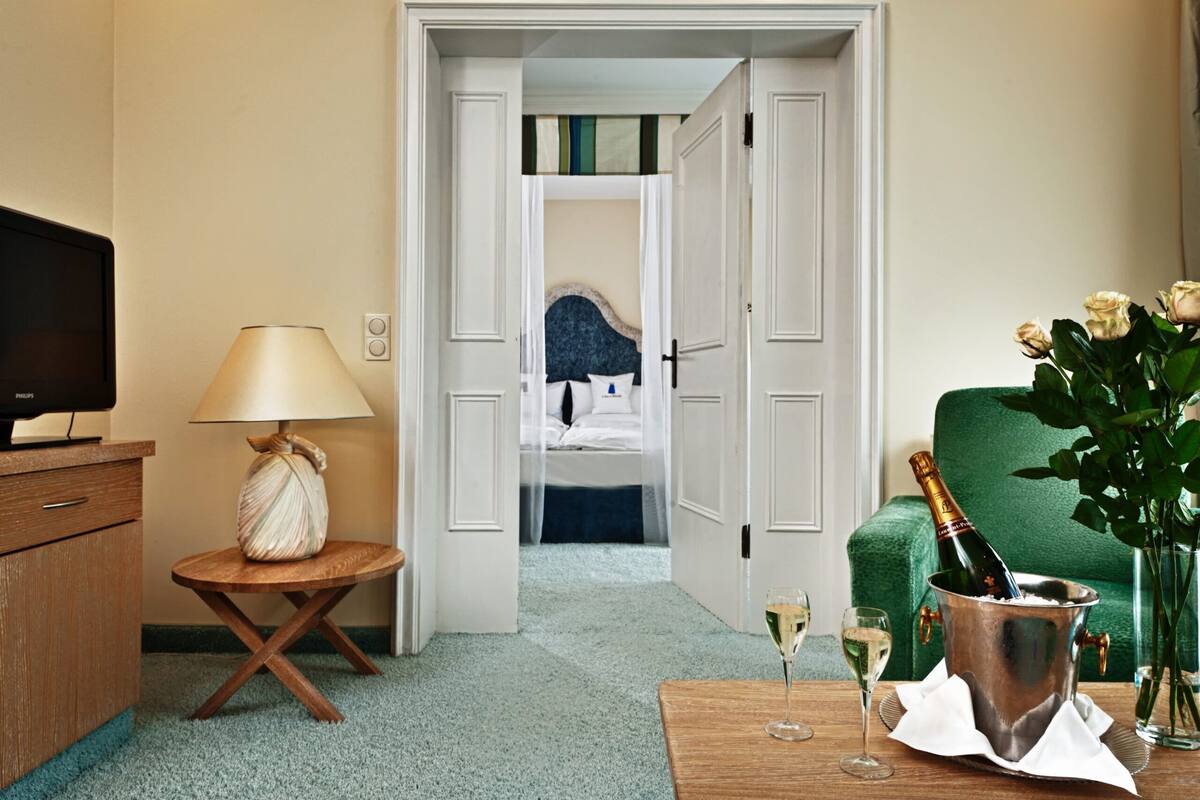 A hotel room with a bed, a television, a lamp, a bottle of champagne, and a vase with flowers.