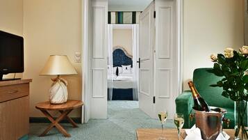 Ein Hotelzimmer mit Bett, Fernseher, Lampe, einer Champagnerflasche und einer Vase mit Blumen.