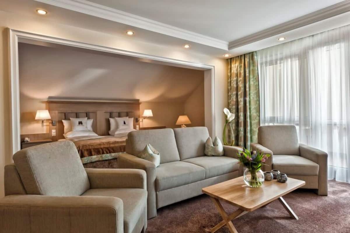 A hotel room with a bed, two sofas, a coffee table, and a large window with curtains.