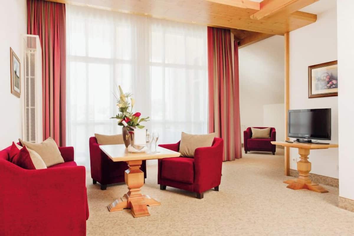 A hotel room with a dining table, red sofas, a TV, and a large window with curtains.