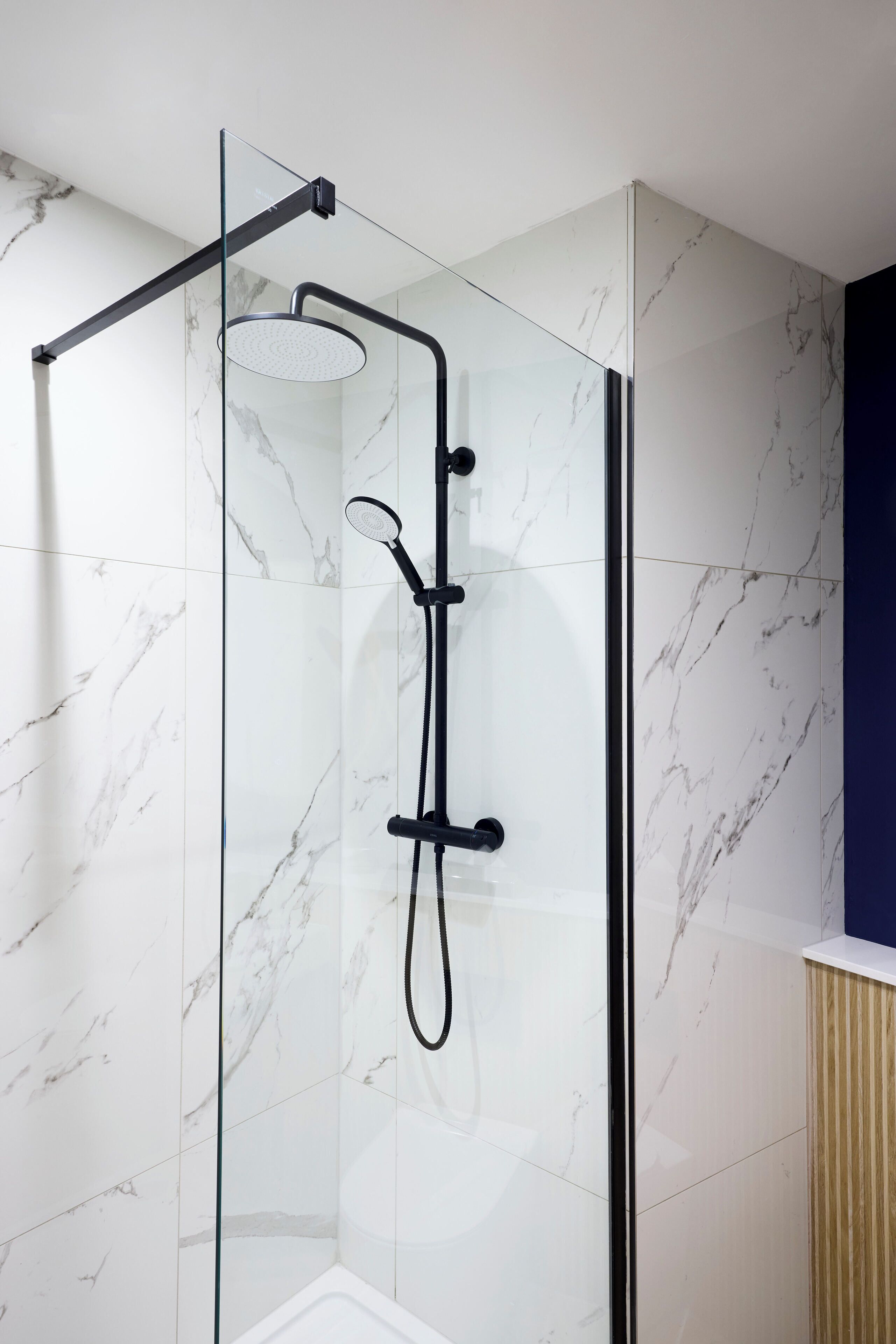 A glass-enclosed shower with a handheld showerhead and a handheld shower nozzle.
