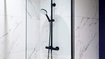 A glass-enclosed shower with a handheld showerhead and a handheld shower nozzle.