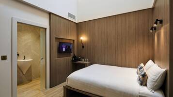 A modern hotel room with a bed, a TV, a bedside table, and a bathroom with a sink and mirror.