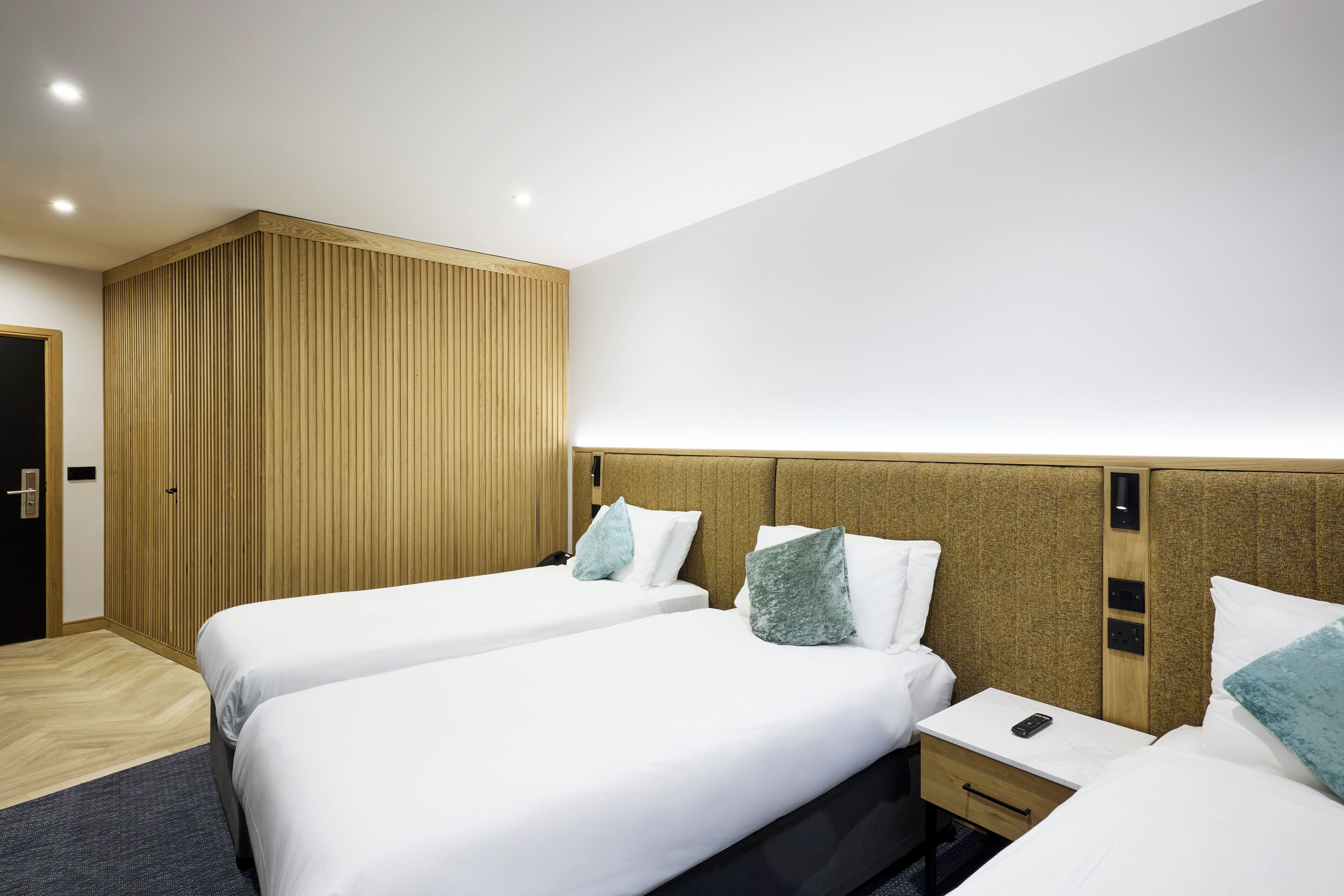 A hotel room with two beds, wooden headboards, a small bedside table with a phone, and a wooden panel wall.