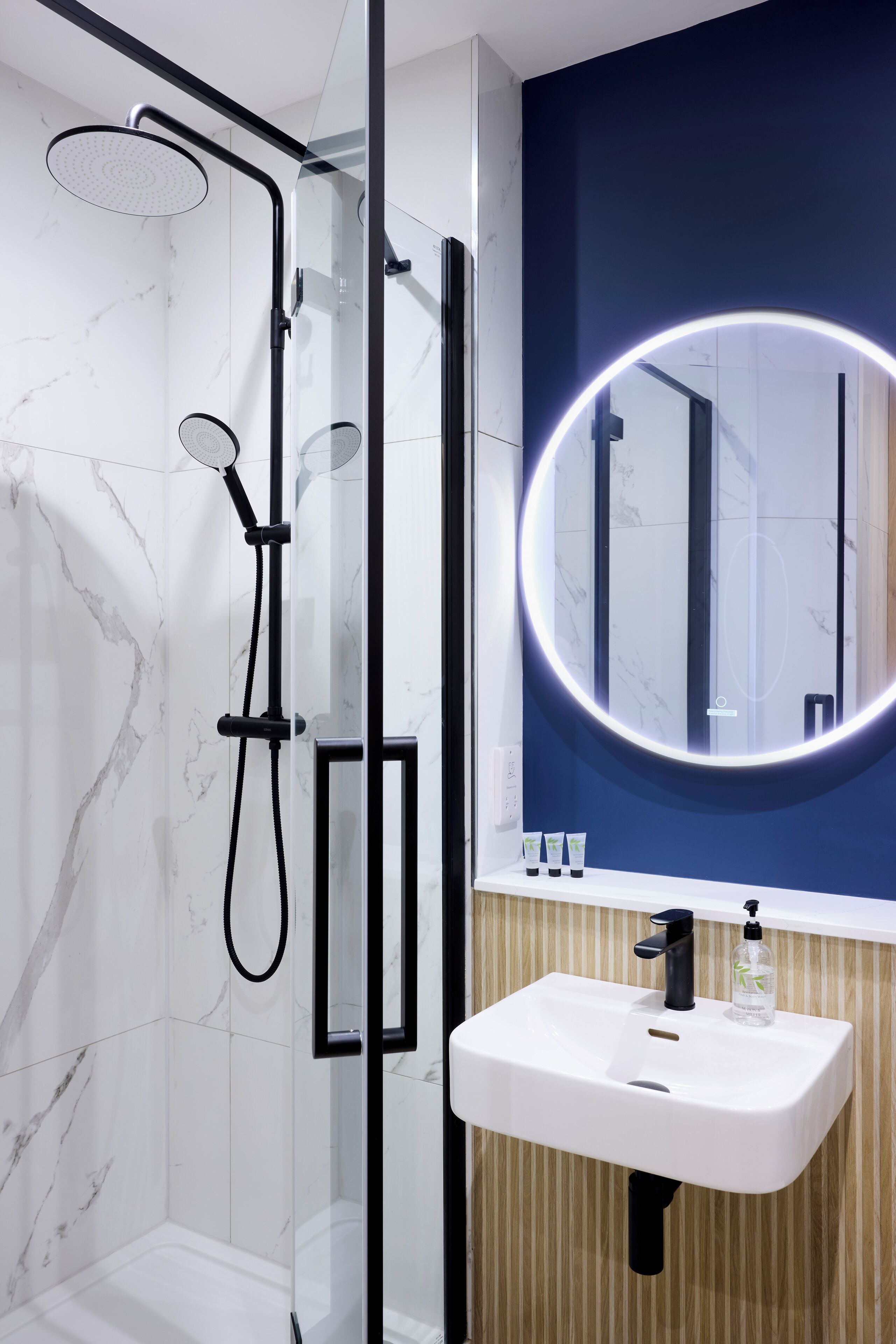 Un baño moderno con ducha envuelta en vidrio, un lavabo blanco con espejo y una pared de acento azul.