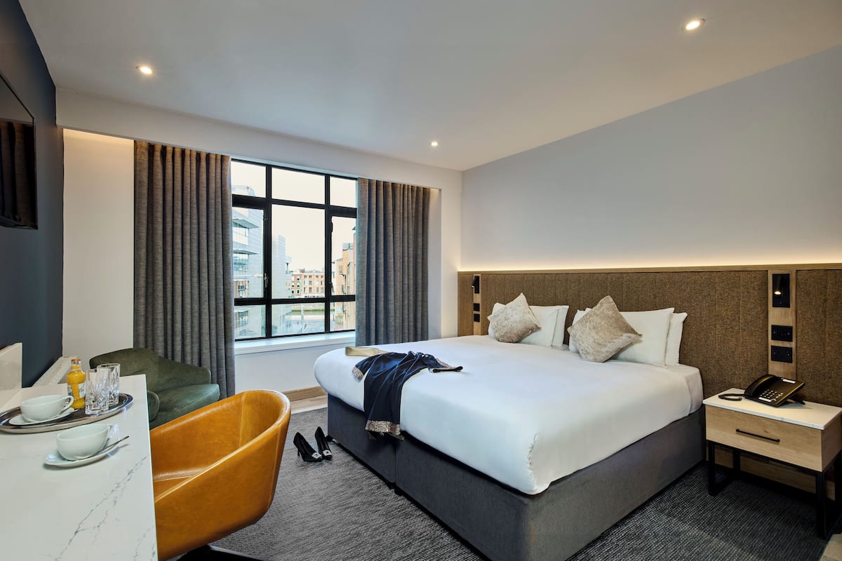 Habitación de hotel moderna con una cama grande, un escritorio con una silla, un sofá y vistas de la ciudad a través de la ventana.
