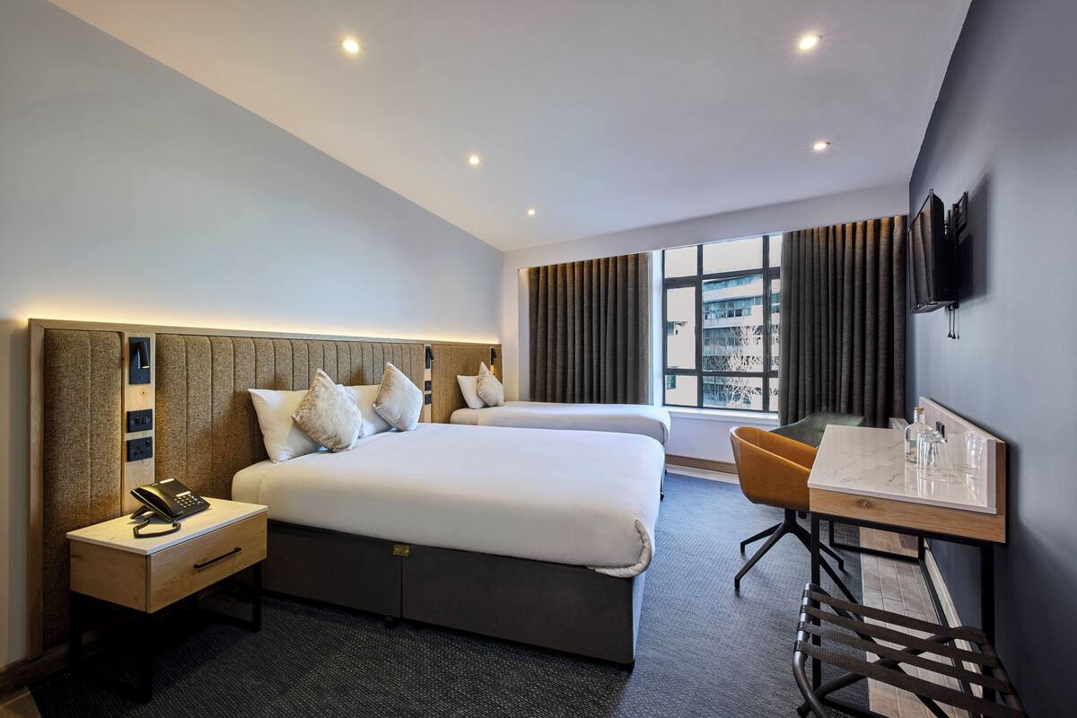 Habitación de hotel con dos camas, un escritorio, una silla, un televisor y una ventana con cortinas.