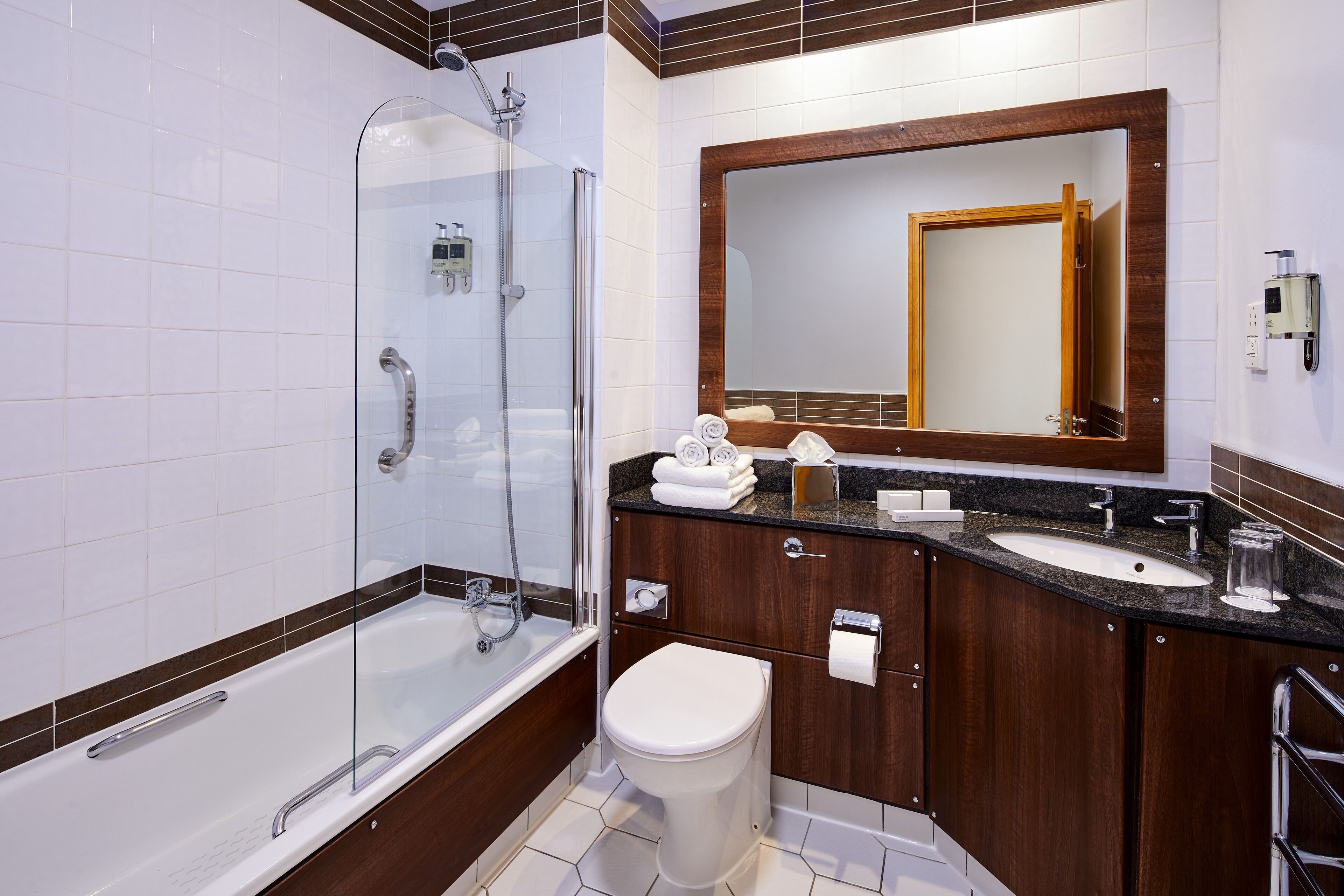 A modern bathroom with a glass-enclosed shower, a white toilet, and a wooden vanity with a sink and mirror.
