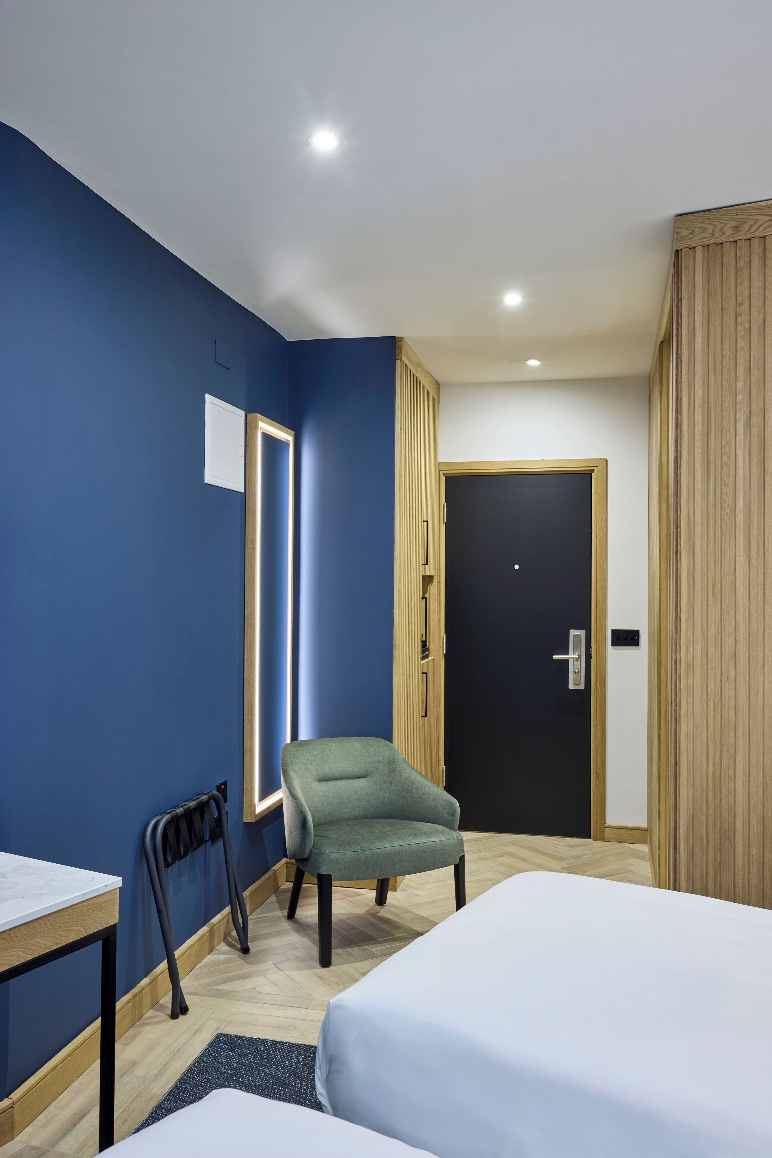 A hotel room with a bed, a chair, a desk, and a door.