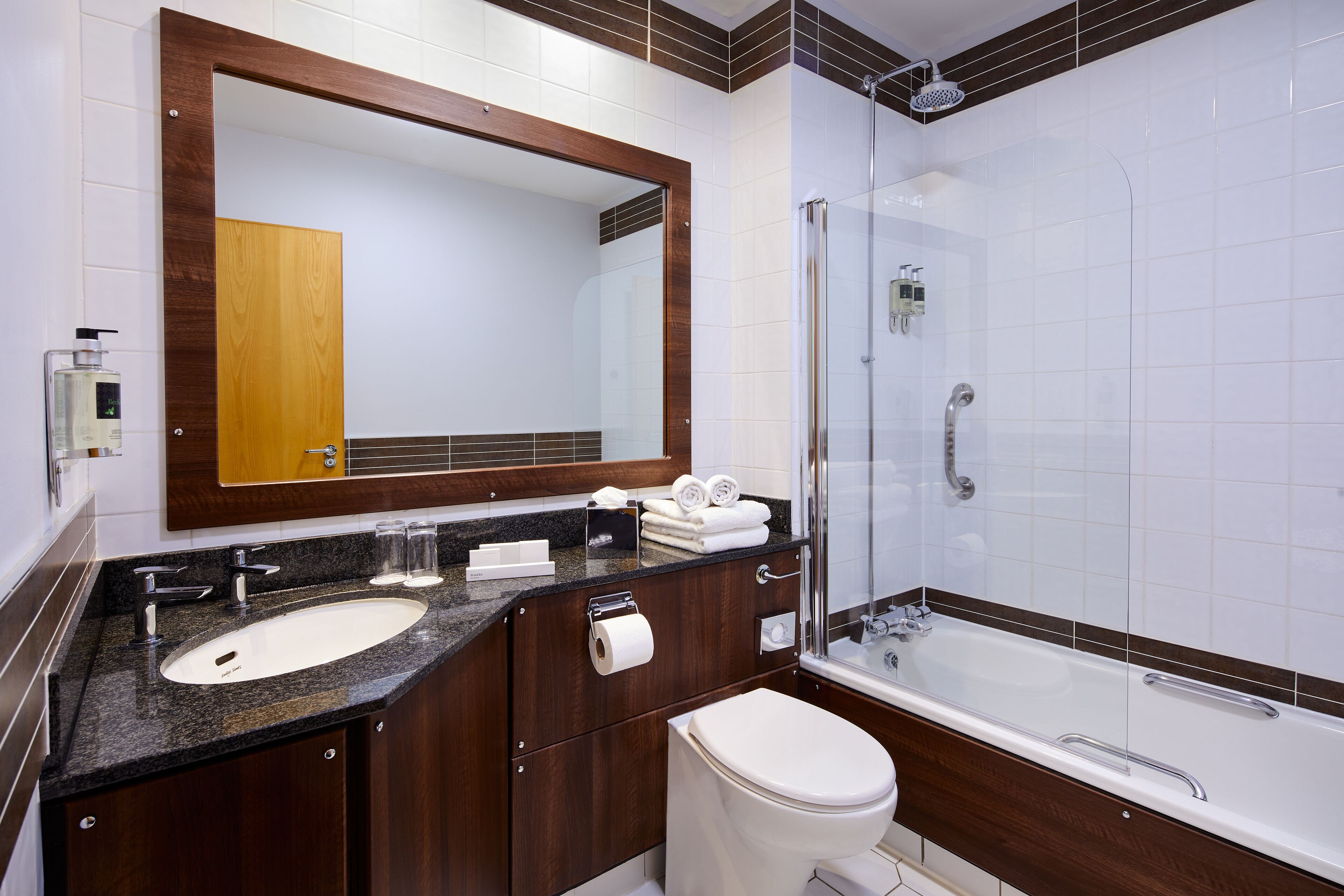 A modern bathroom with a large mirror, a sink, a toilet, and a bathtub.