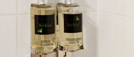 Two bottles of BeeKind shower gel and conditioner on a white tiled wall.
