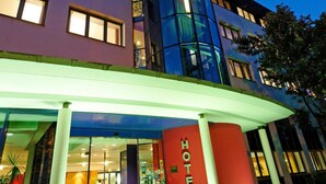 A hotel entrance with a glass facade, a red sign, and a covered walkway.