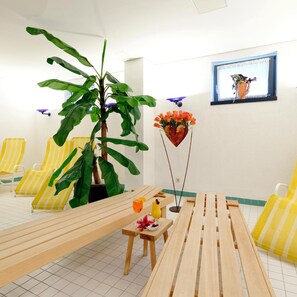 A room with striped yellow chairs, a wooden table, a potted plant, a wall-mounted picture, and a floor lamp.