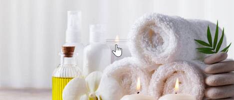 A spa setting with a towel, candles, a bottle of oil, and a flower.