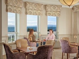 Una habitación con ventanas amplias, una mesa, sillas y vista al mar.
