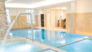 An indoor swimming pool with clear water, a tiled deck, and a stone wall on one side.