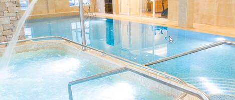 Una piscina interior con agua cristalina, un borde de baldosas y una pared de piedra en un lateral.