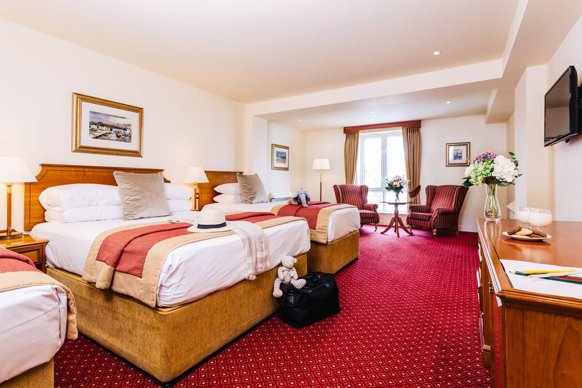 A hotel room with two beds, a desk, a chair, a TV, and a window with curtains.