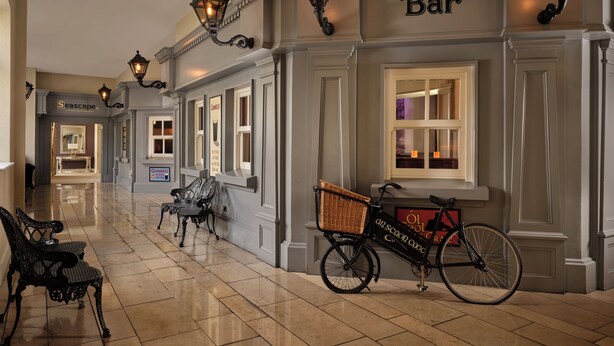 A hallway with a bar, wicker chairs, a bicycle with a basket, and ornate wall sconces.