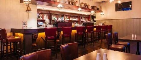 Una zona de bar con mobiliario de madera, sillas rojas y una barra con diversas botellas.