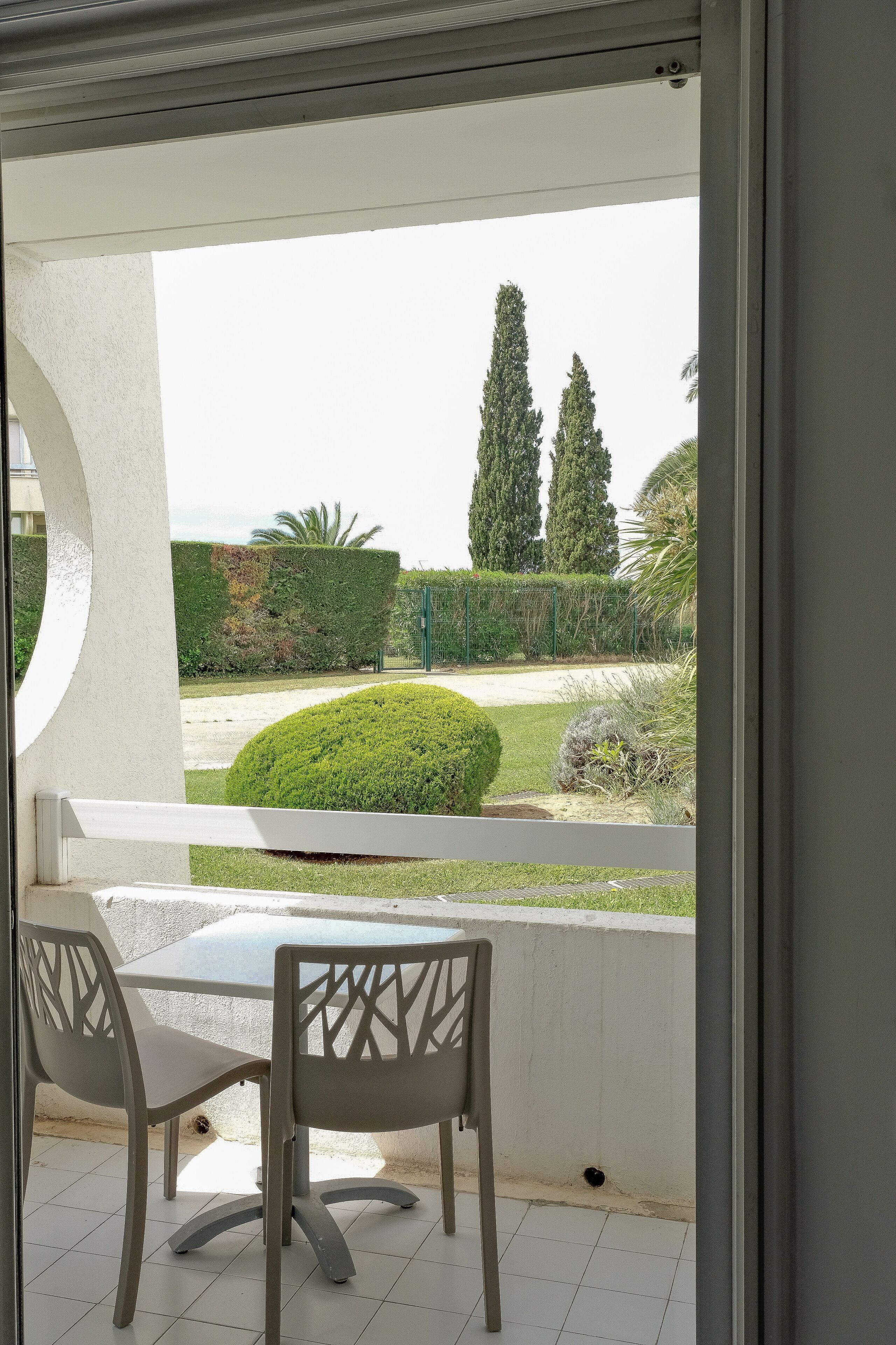 Un patio exterior con una mesa y sillas, y vistas a un jardín bien cuidado con setos y árboles.