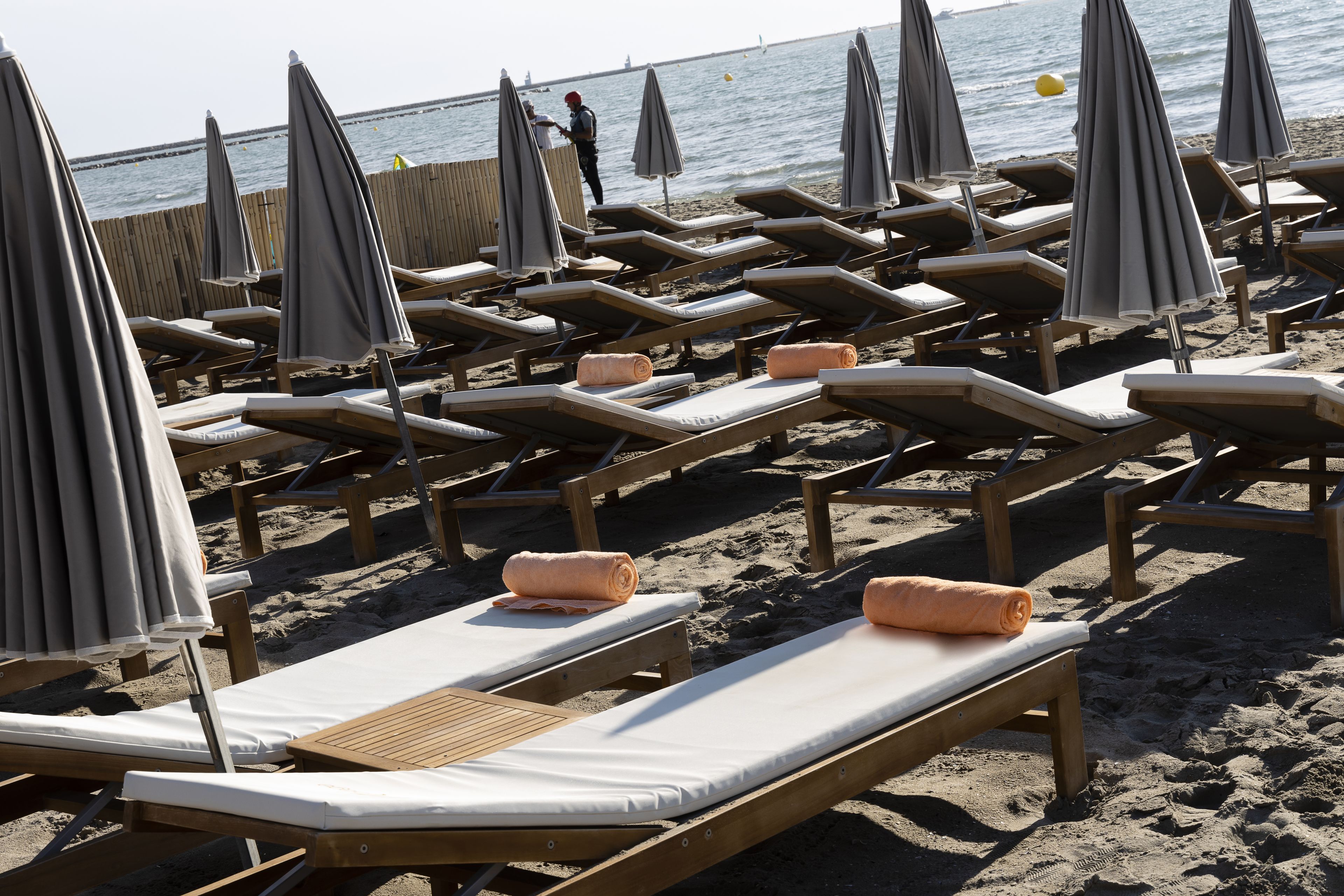 Rows of wooden lounge chairs with grey umbrellas on a sandy beach.
