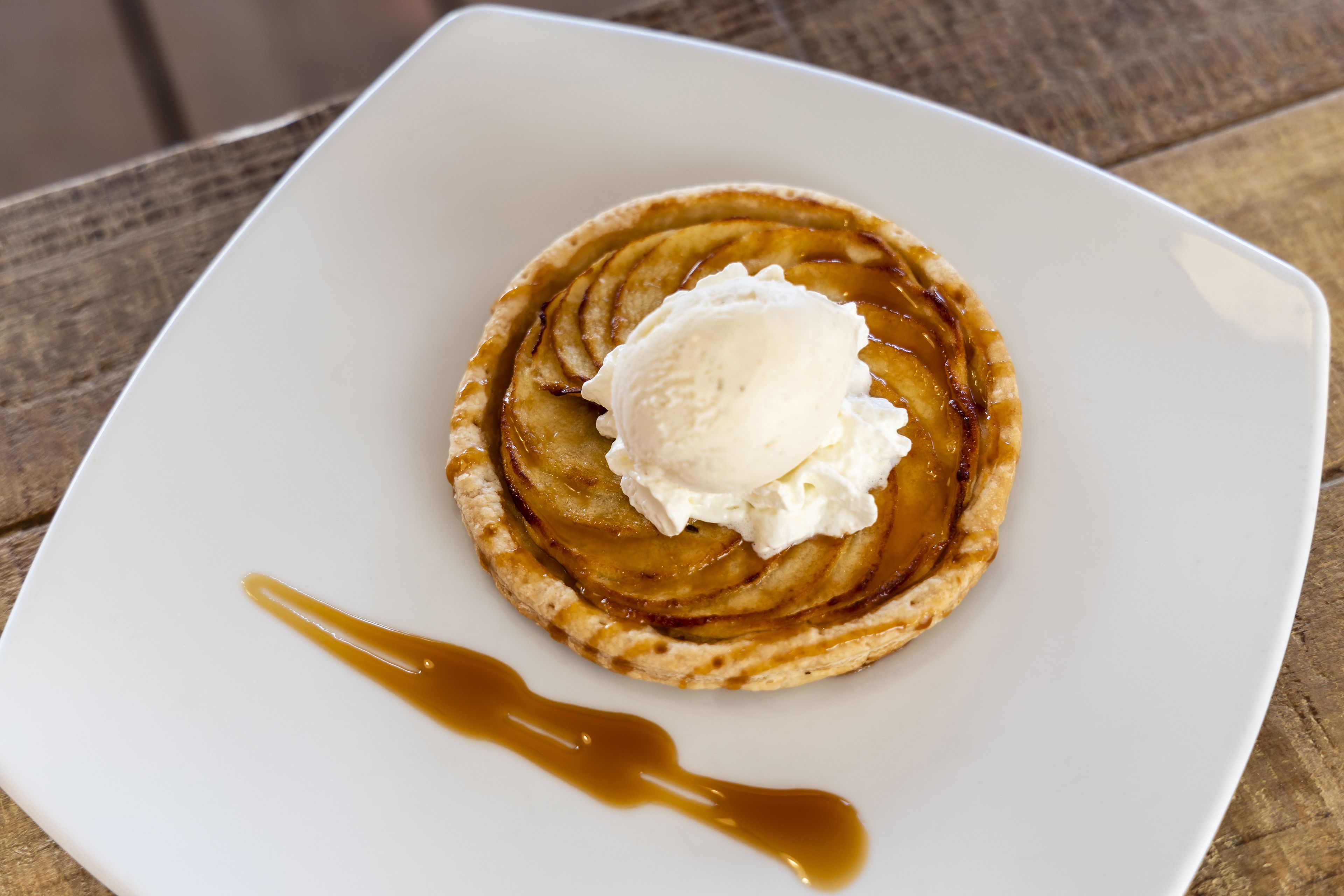 Postre sobre un plat blanc amb salsa de caramel i una bola de gelat.
