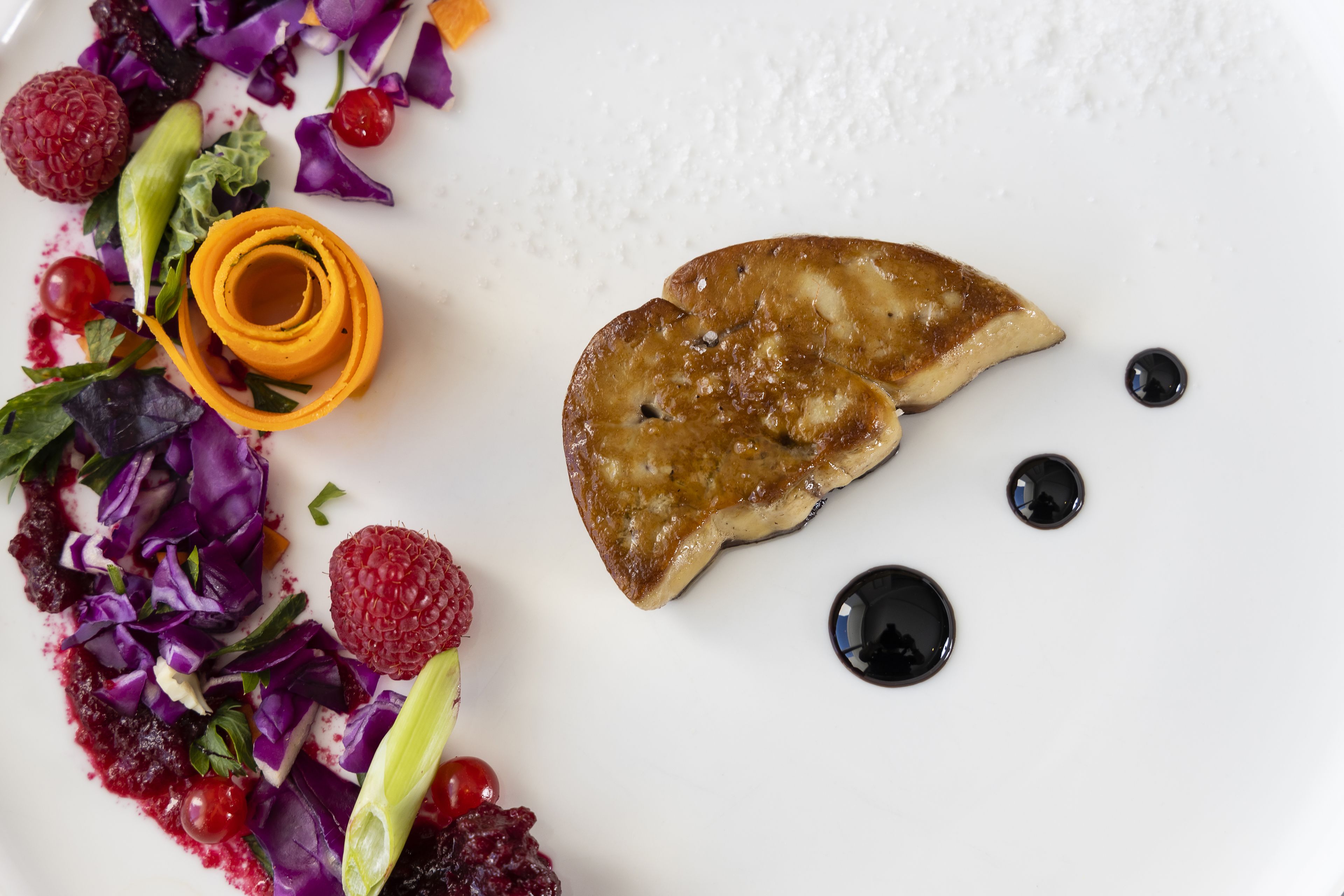 Une assiette blanche contenant un morceau de nourriture, peut-être une pâtisserie, et une salade colorée composée de divers légumes et de baies.