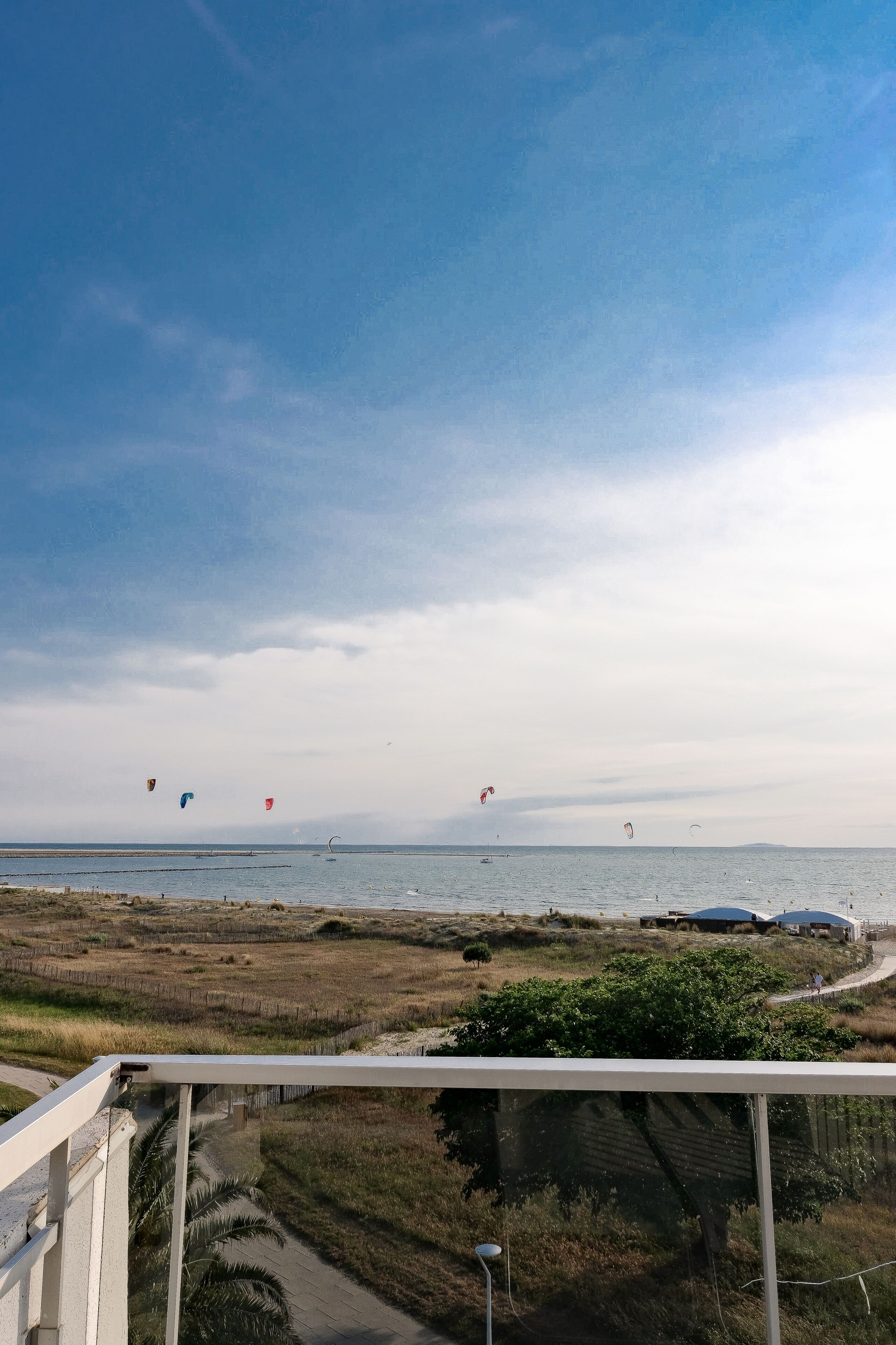 A view from a balcony overlooking a beach with kites flying in the sky.