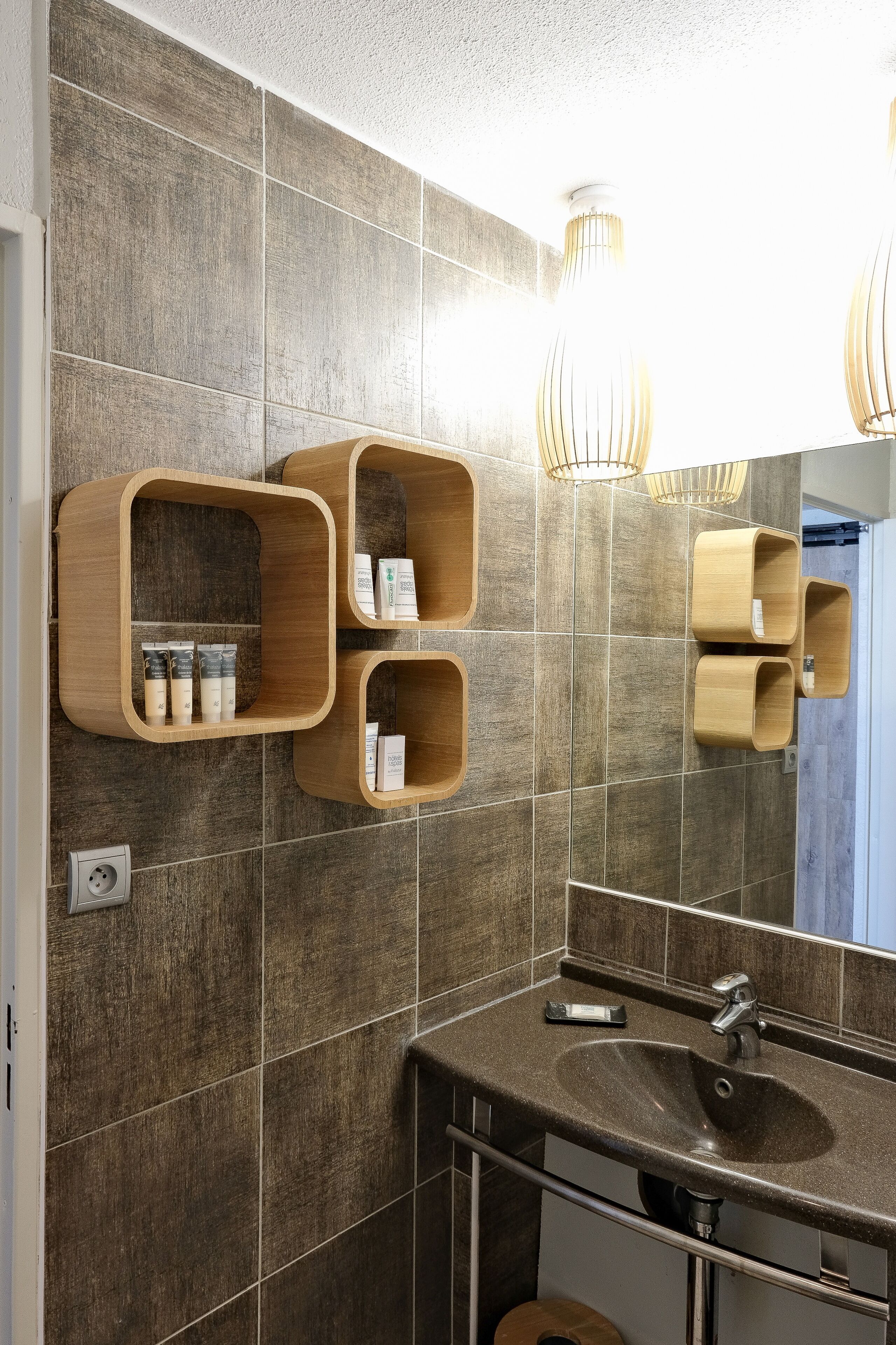 Ein modernes Badezimmer mit Holzregalen, auf denen Pflegeprodukte stehen, einem großen Spiegel und einem Waschbecken.
