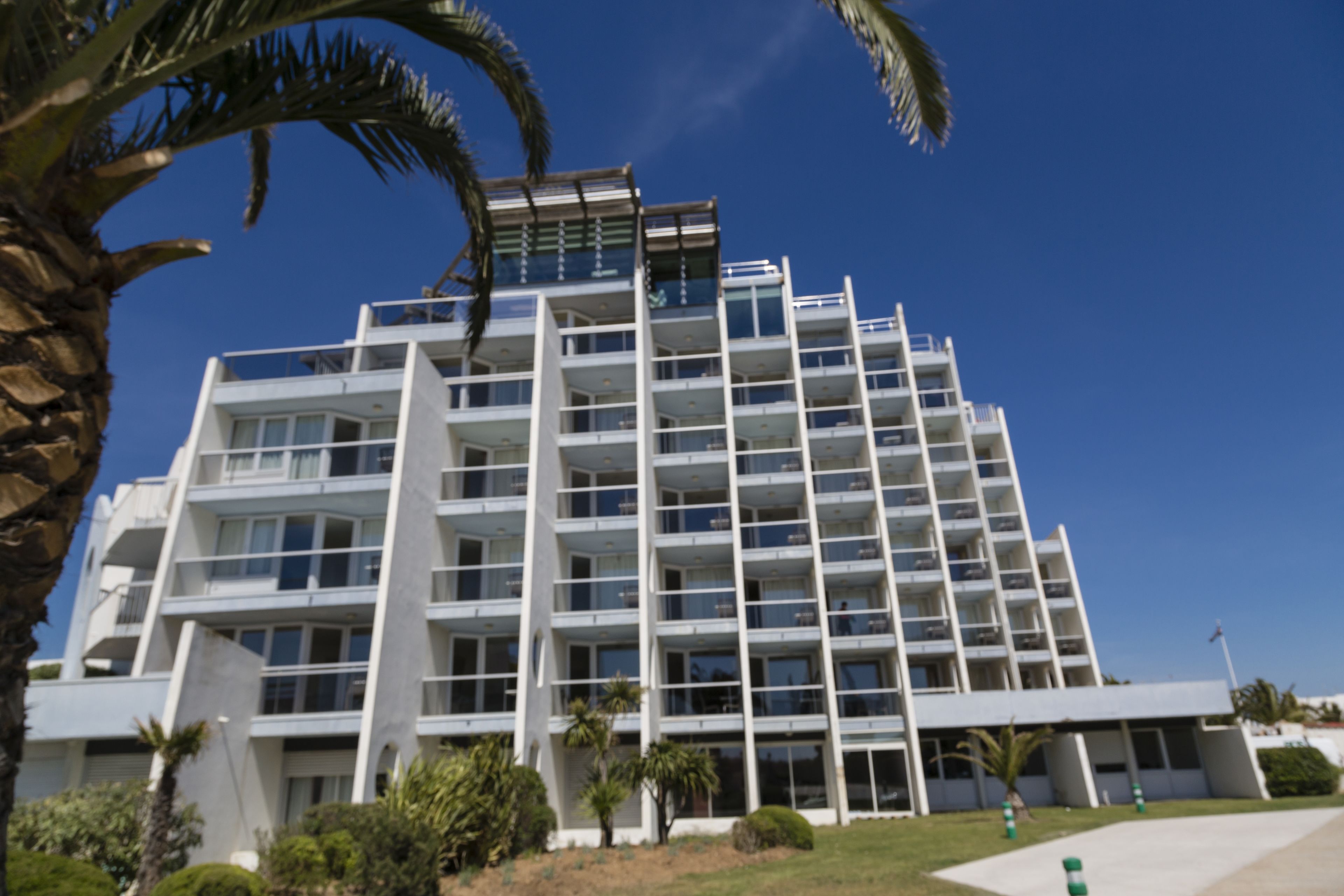 A multi-story hotel with a modern architectural design, featuring balconies on each floor and a central courtyard.