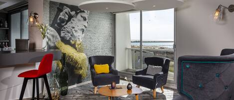 A modern living room with a large window, a bar area, and a mural.