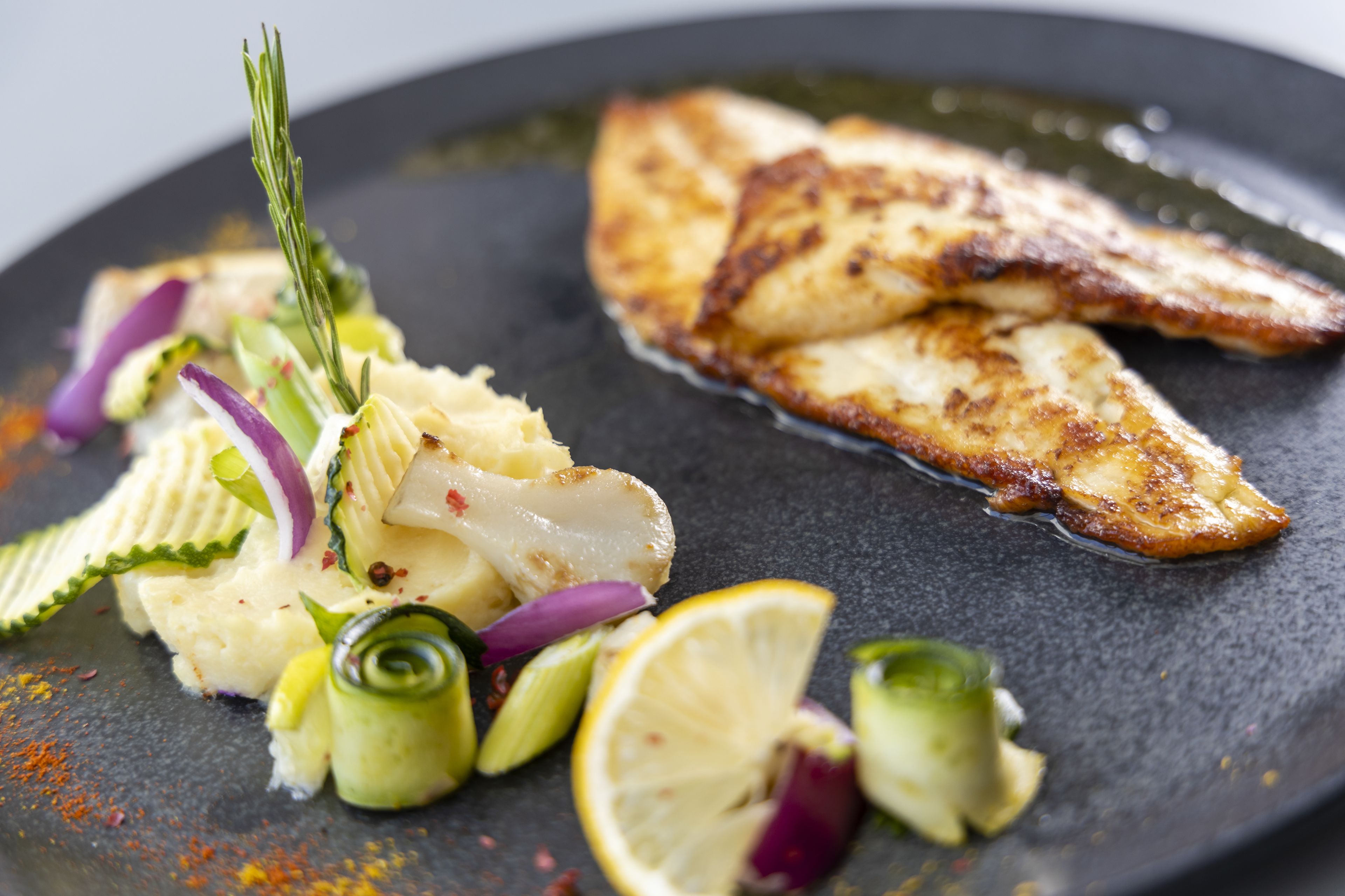 A plate with grilled fish, vegetables, and a lemon slice.