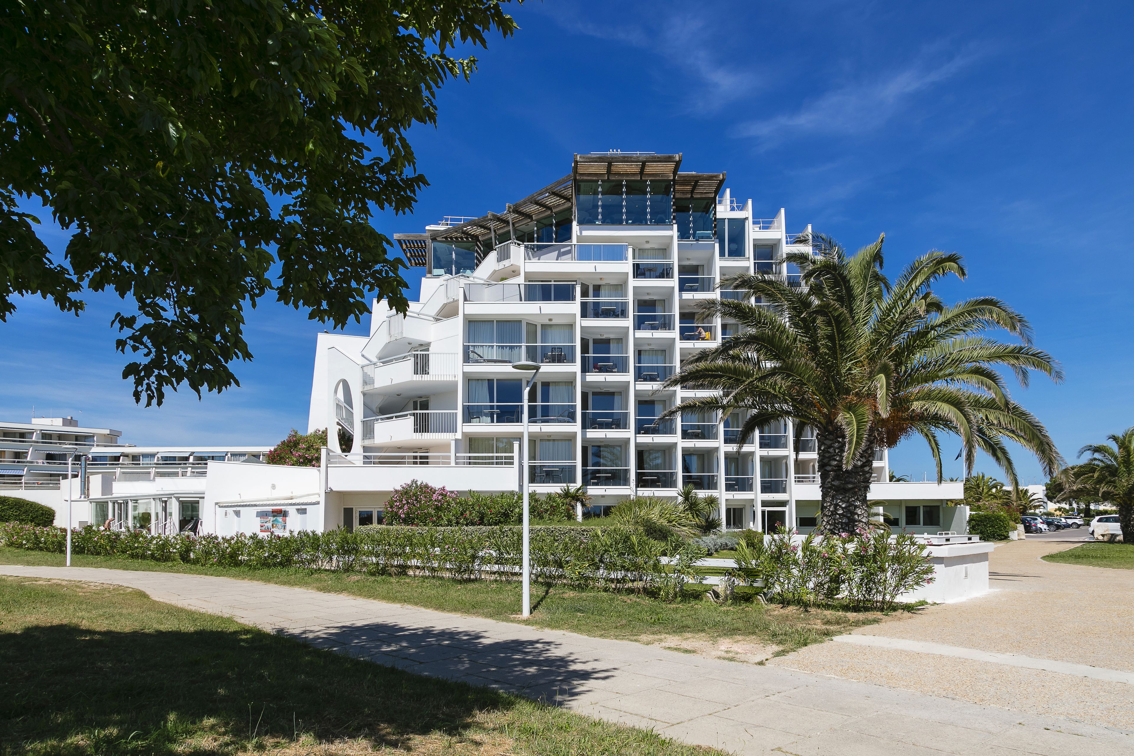 Un hôtel à plusieurs étages doté de balcons, d’un palmier et surplombant un ciel bleu azur.