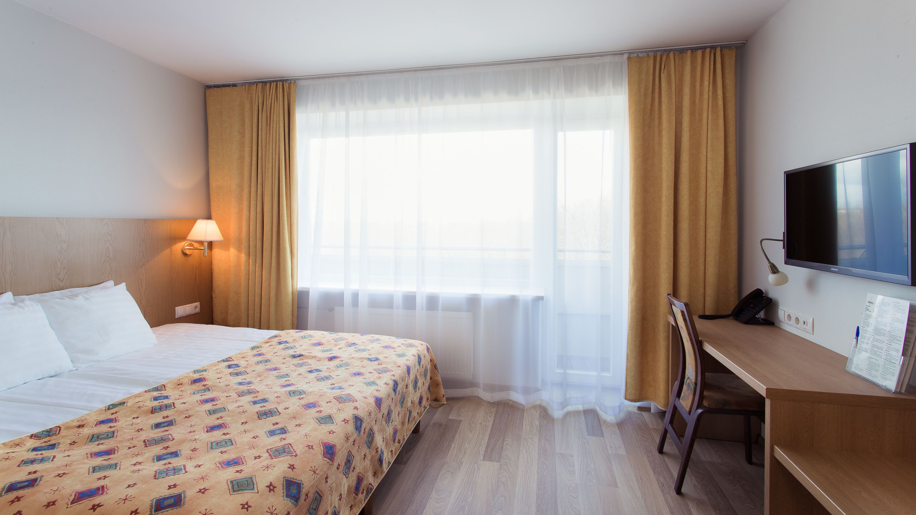 Une chambre d’hôtel avec un lit, un bureau, une télévision et une fenêtre avec des rideaux.