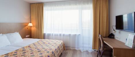 Une chambre d’hôtel avec un lit, un bureau, une télévision et une fenêtre avec des rideaux.