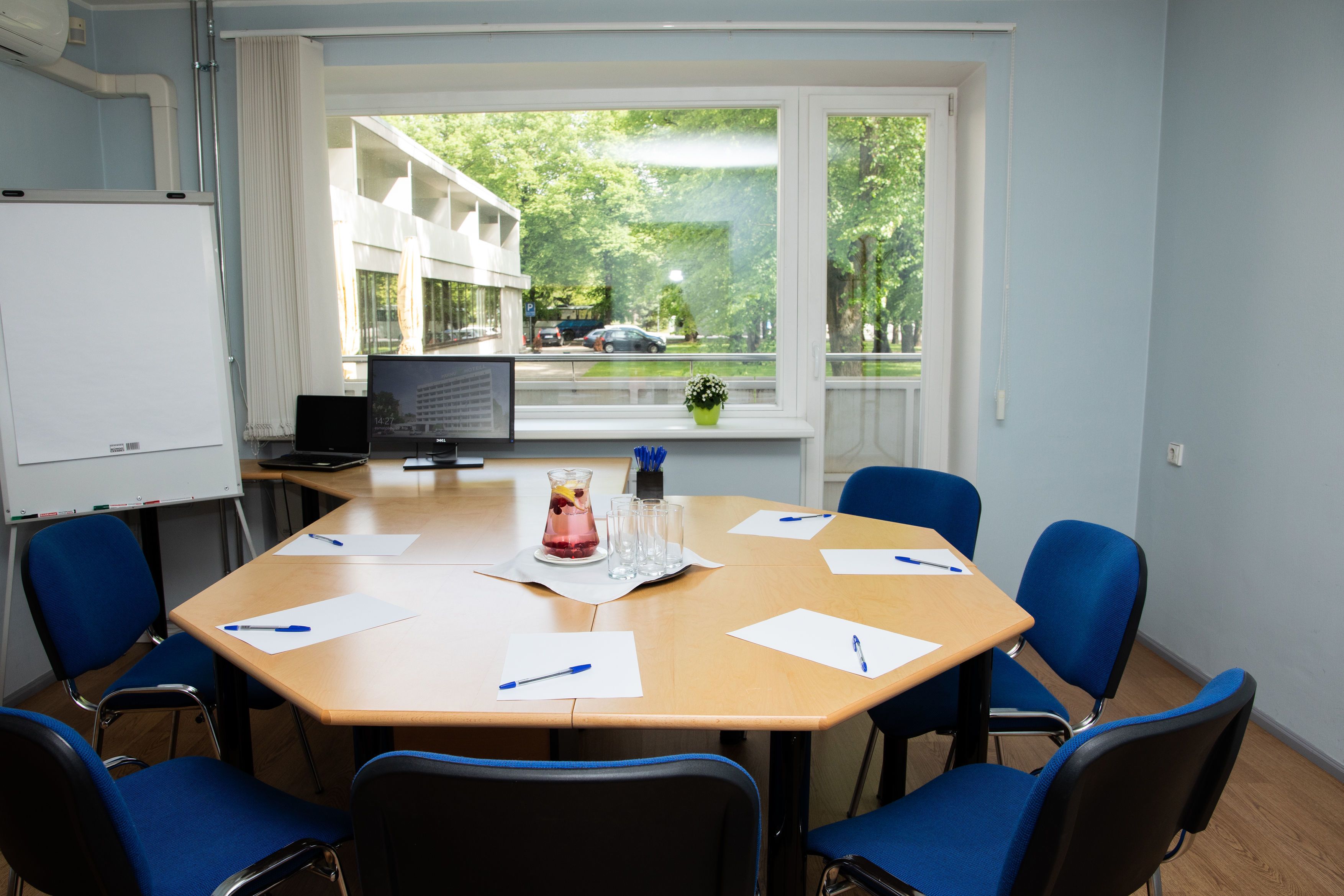 A conference room with a large table, blue chairs, a whiteboard, and a view of a street with cars and trees.