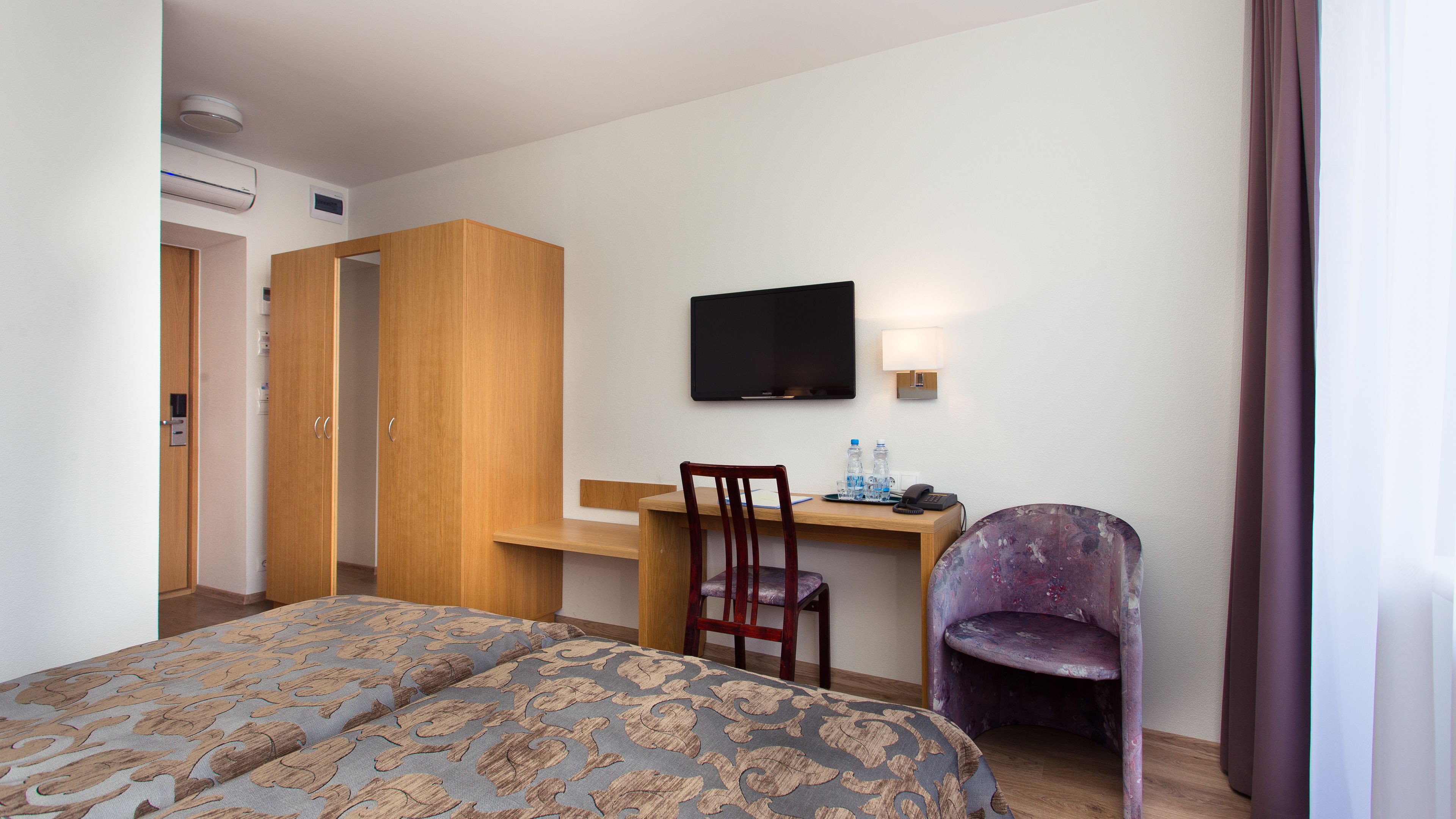 Una habitació d'hotel amb un llit, una taula de treball, una cadira, un televisor i un armari.
