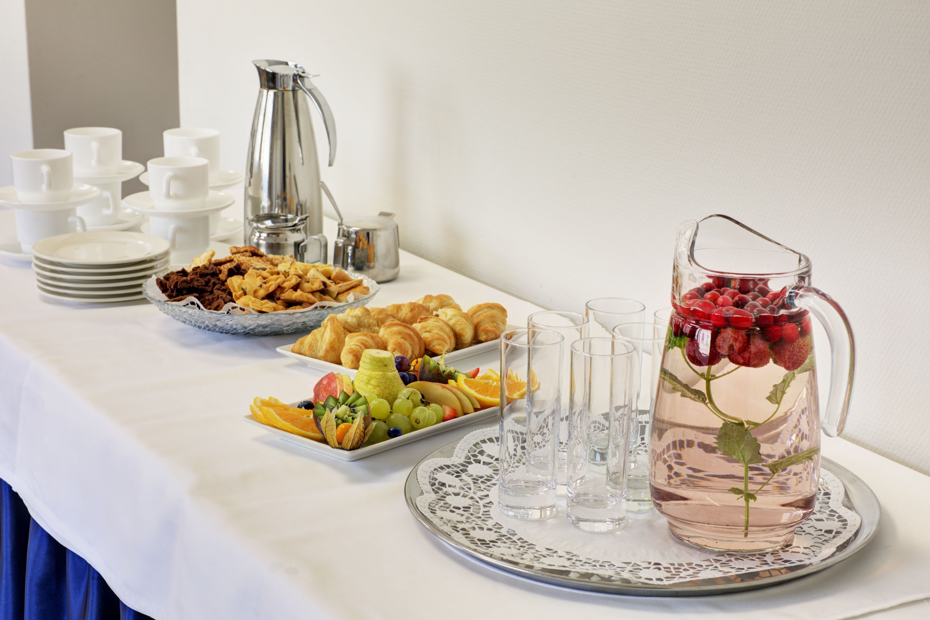 A breakfast buffet with croissants, fruits, and a pitcher of water with strawberries.