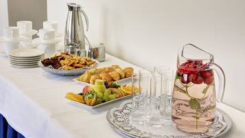 A breakfast buffet with croissants, fruits, and a pitcher of water with strawberries.