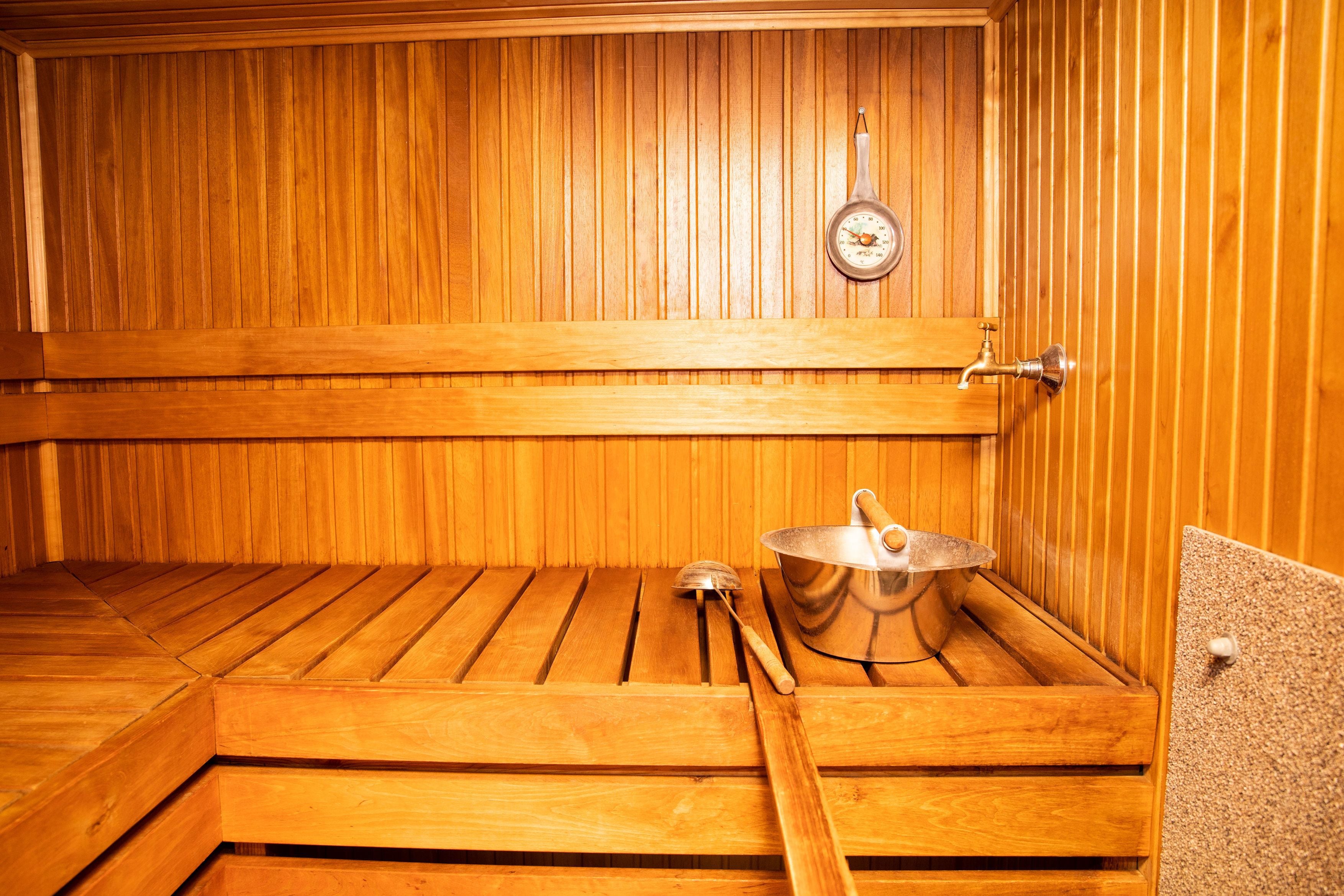 A sauna with wooden benches, a metal basin, and a thermometer on the wall.