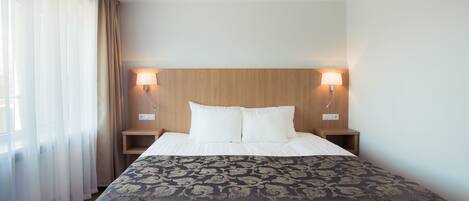 A neatly made bed with a patterned bedspread, two bedside lamps, and a wooden headboard in a hotel room.
